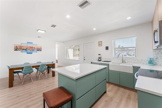 2715 Herwald St, Sarasota, FL 34231 - kitchen featuring green cabinets, a kitchen island, light wood finished floors, a sink, and light countertops