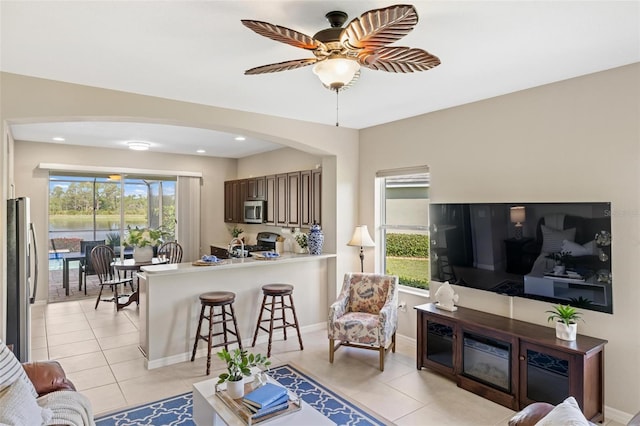 living area featuring light tile patterned floors, arched walkways, a ceiling fan, recessed lighting, and baseboards