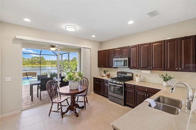 kitchen featuring appliances with stainless steel finishes, a sink, decorative backsplash, dark brown cabinets, and baseboards