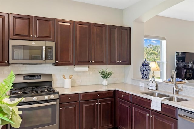 kitchen featuring stainless steel appliances, a sink, tasteful backsplash, and reddish brown cabinets