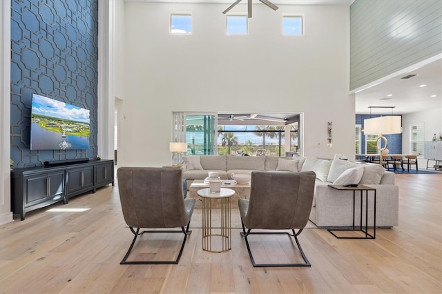 living room featuring a high ceiling, light wood finished floors, plenty of natural light, and ceiling fan