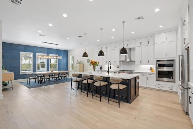 kitchen with appliances with stainless steel finishes, wall chimney range hood, a breakfast bar, recessed lighting, and white cabinetry