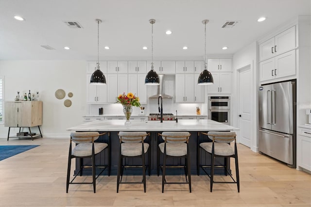 kitchen with stainless steel appliances, wall chimney exhaust hood, white cabinetry, backsplash, and light wood-style floors