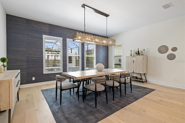 dining area featuring baseboards, light wood-style floors, a chandelier, and an accent wall