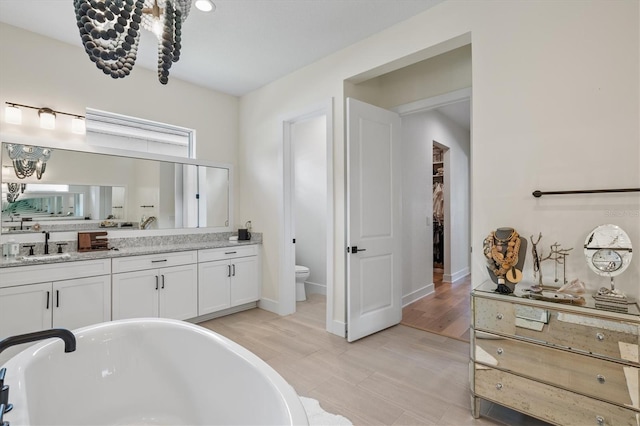 full bathroom with toilet, a soaking tub, vanity, and a walk in closet
