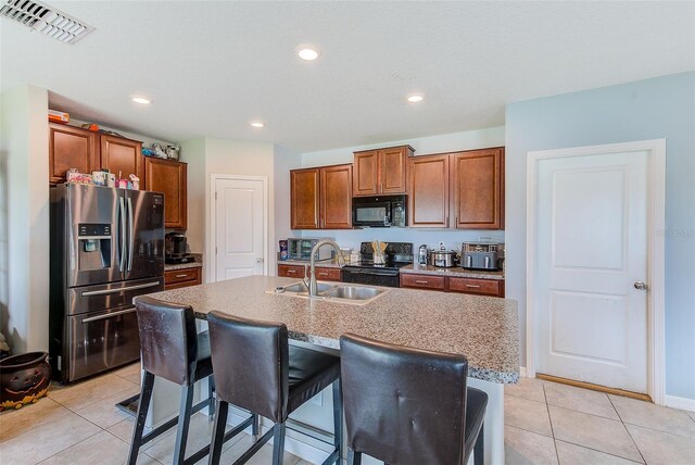 10944 Rainbow Pyrite Dr, Wimauma, FL 33598 - kitchen with black appliances, a sink, light tile patterned floors, a breakfast bar, and a kitchen island with sink
