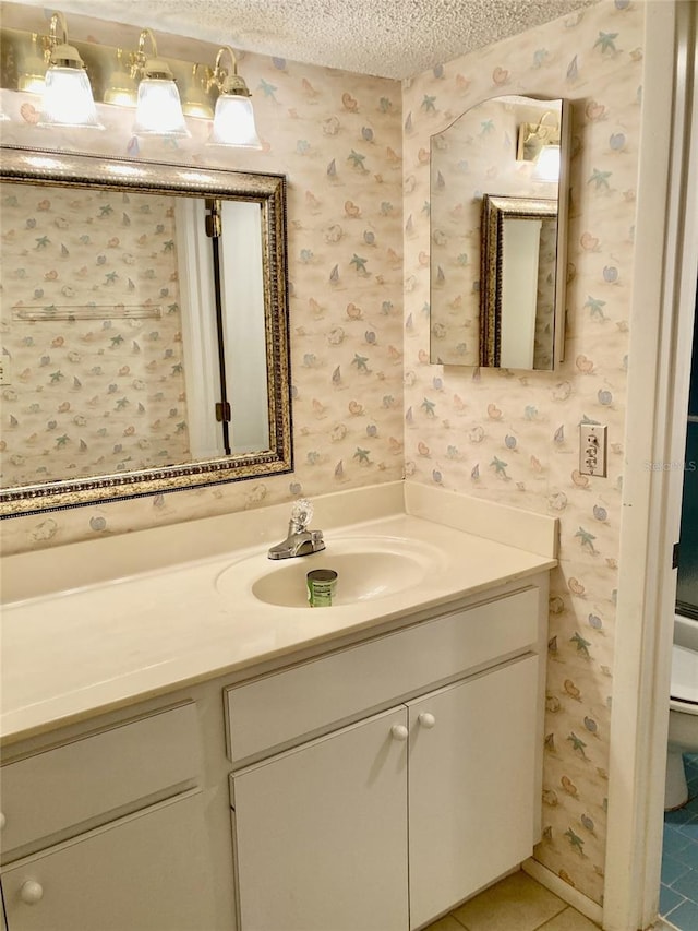 6124 43rd St W Unit 104A, Bradenton, FL 34210 - bathroom featuring wallpapered walls, a textured ceiling, vanity, toilet, and tile patterned floors