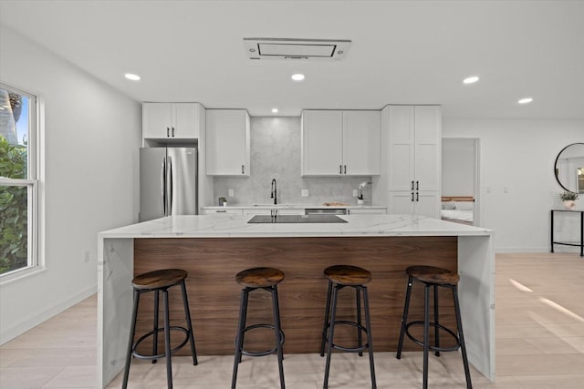 kitchen with freestanding refrigerator, a sink, white cabinets, decorative backsplash, and a kitchen breakfast bar
