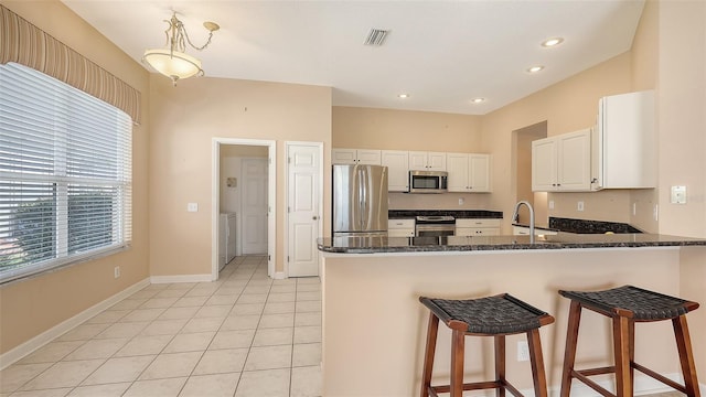 4274 Tennyson Way, Venice, FL 34293 - kitchen featuring appliances with stainless steel finishes, white cabinetry, washing machine and clothes dryer, a peninsula, and dark stone counters