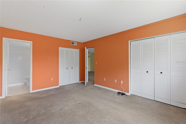 unfurnished bedroom with two closets, carpet flooring, baseboards, and connected bathroom