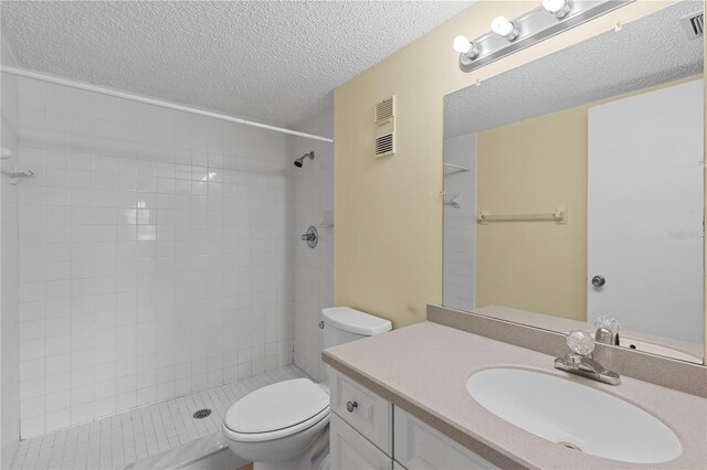 bathroom featuring a textured ceiling, toilet, vanity, and tiled shower