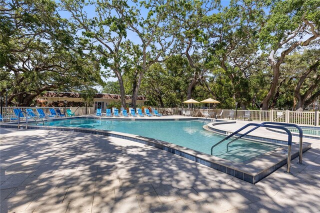 community pool with fence, a patio area, and view of scattered trees