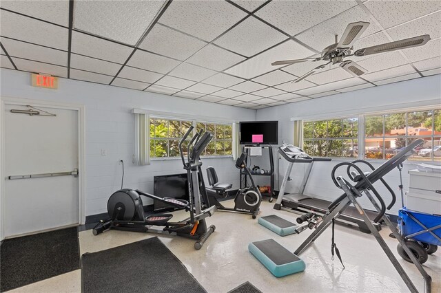 workout room with a paneled ceiling, a ceiling fan, and concrete block wall