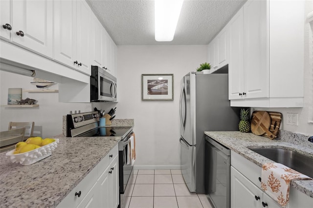5681 Midnight Pass Rd Unit 104, Sarasota, FL 34242 - kitchen with appliances with stainless steel finishes, a textured ceiling, white cabinetry, baseboards, and light tile patterned floors