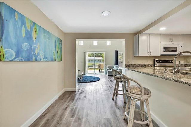 7308 Maryland Ave, Hudson, FL 34667 - kitchen featuring white microwave, dark stone countertops, light wood-style flooring, a breakfast bar, and baseboards