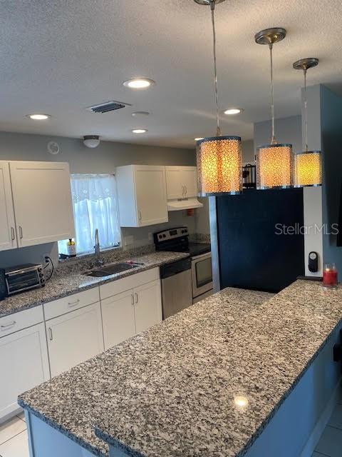 kitchen with a sink, stainless steel appliances, under cabinet range hood, a textured ceiling, and white cabinetry