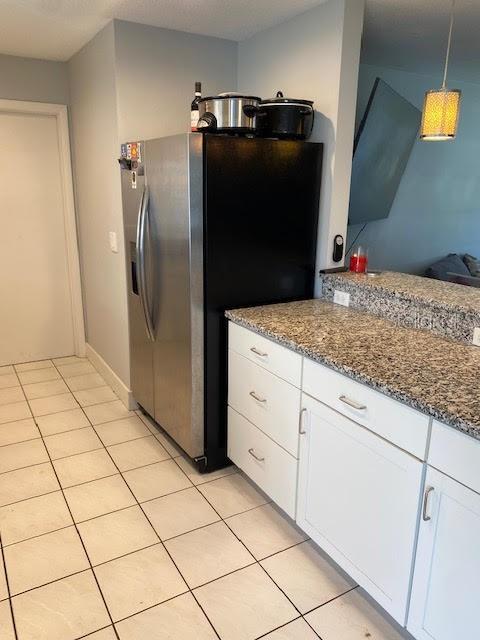 kitchen featuring stainless steel fridge, white cabinets, light tile patterned flooring, dark stone countertops, and pendant lighting