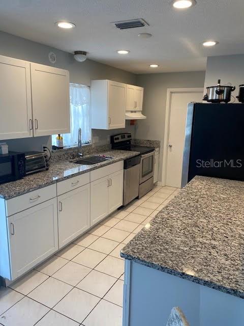 kitchen with appliances with stainless steel finishes, a sink, under cabinet range hood, white cabinets, and dark stone countertops