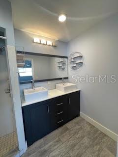 full bath with double vanity, baseboards, and a shower