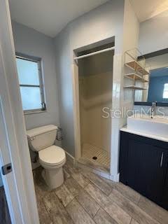 full bathroom with wood finished floors, a shower stall, toilet, and vanity