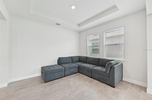 living area with a tray ceiling, baseboards, and light tile patterned floors