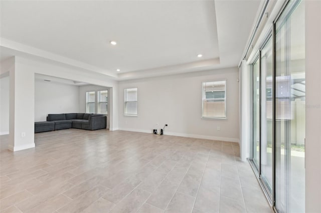 unfurnished living room with a raised ceiling, plenty of natural light, baseboards, and recessed lighting