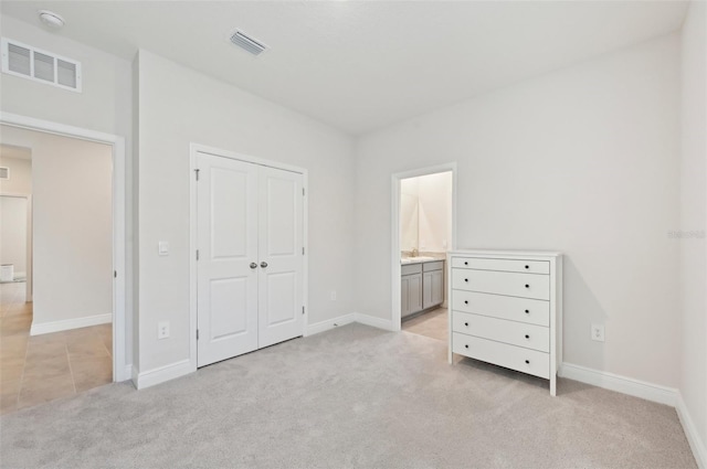 unfurnished bedroom featuring light colored carpet, baseboards, a sink, a closet, and ensuite bath