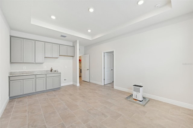 kitchen featuring gray cabinets, a raised ceiling, a sink, recessed lighting, and baseboards