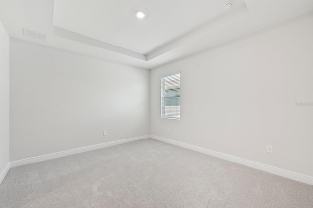 spare room featuring light carpet, baseboards, a raised ceiling, and recessed lighting