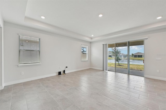 unfurnished room featuring a tray ceiling, recessed lighting, and baseboards