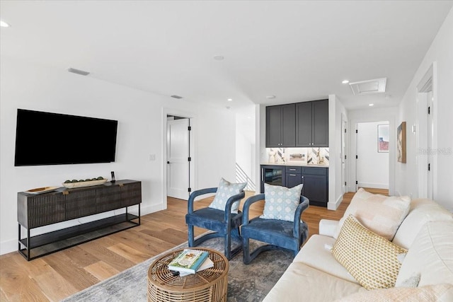 living room featuring light wood-style flooring, recessed lighting, beverage cooler, baseboards, and attic access