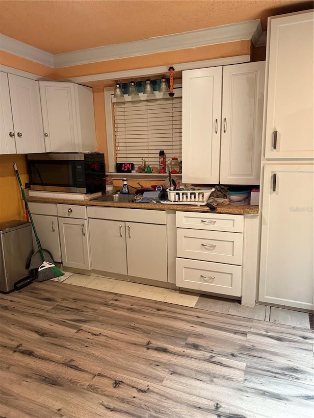 3720 27th St E, Bradenton, FL 34208 - kitchen featuring stainless steel microwave, crown molding, light wood-style floors, white cabinets, and dark countertops