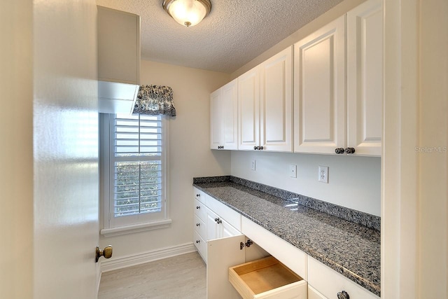 5812 Garden Lakes Fern, Bradenton, FL 34203 - kitchen with a textured ceiling, white cabinetry, dark stone counters, light wood finished floors, and baseboards
