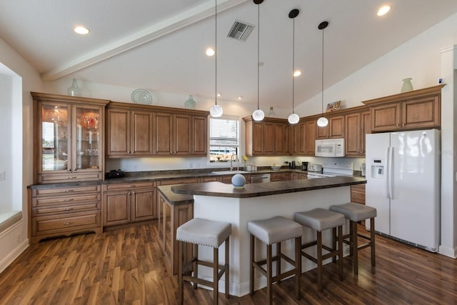 kitchen with white appliances, dark countertops, brown cabinetry, a sink, and a breakfast bar area