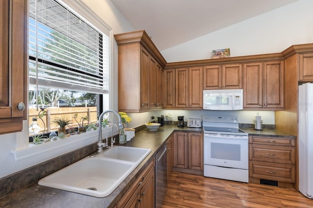 kitchen featuring white appliances, a sink, lofted ceiling, brown cabinetry, and dark countertops