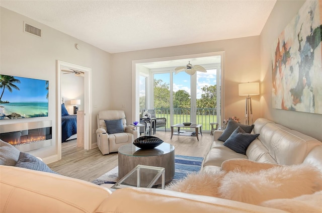 8735 Olde Hickory Ave Unit 8205, Sarasota, FL 34238 - living room with wood finished floors, a glass covered fireplace, a ceiling fan, and a textured ceiling