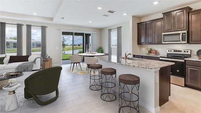 kitchen with stainless steel appliances, a sink, a kitchen bar, light stone countertops, and recessed lighting
