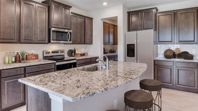 kitchen with stainless steel appliances, a sink, a breakfast bar area, decorative backsplash, and dark brown cabinetry