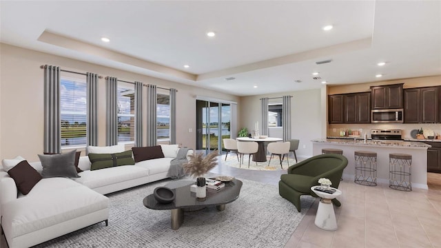 living area with plenty of natural light, a raised ceiling, light tile patterned floors, and recessed lighting