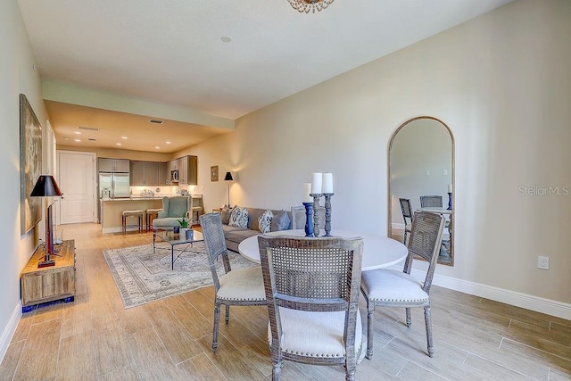 dining area featuring light wood finished floors, baseboards, and arched walkways