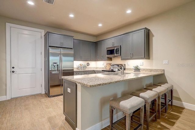kitchen featuring appliances with stainless steel finishes, a sink, a peninsula, light stone countertops, and a breakfast bar area