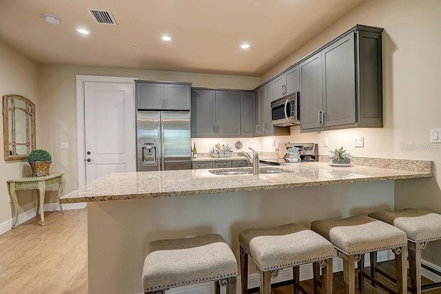 kitchen featuring stainless steel appliances, a sink, a peninsula, light stone counters, and recessed lighting