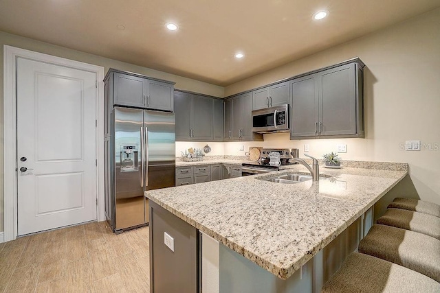 kitchen with appliances with stainless steel finishes, a peninsula, light stone countertops, recessed lighting, and a breakfast bar area