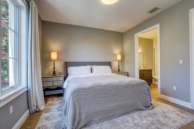 bedroom with wood finished floors, baseboards, and ensuite bathroom