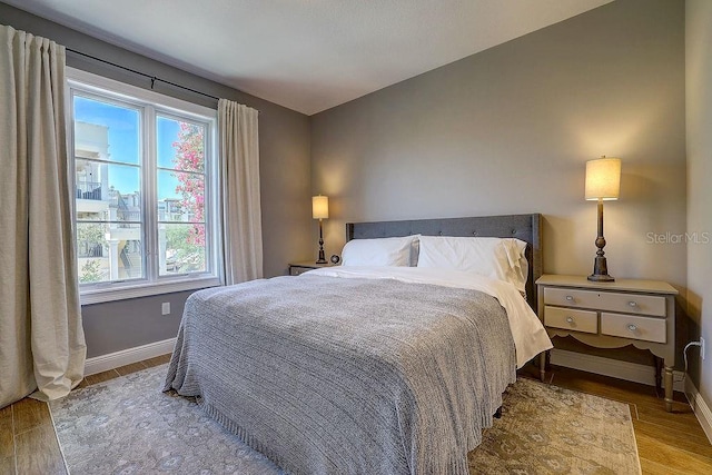 bedroom with baseboards, wood finished floors, and multiple windows