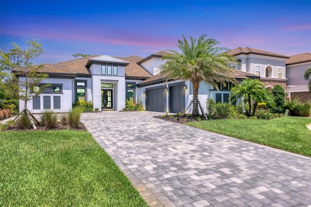 contemporary home with decorative driveway, an attached garage, stucco siding, a front yard, and a tile roof