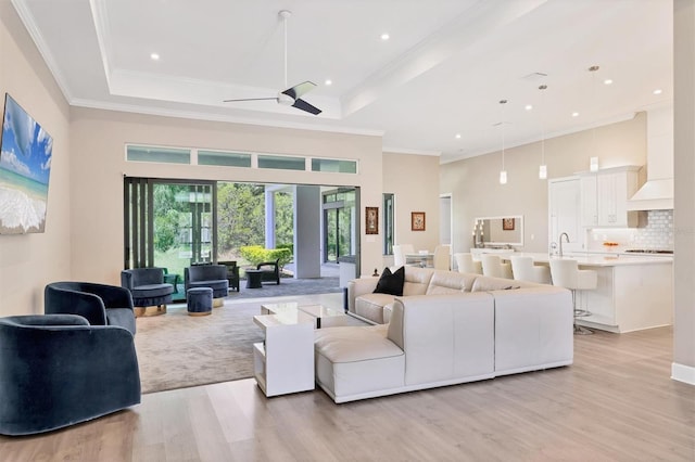 living room featuring ceiling fan, light wood-style flooring, ornamental molding, recessed lighting, and a raised ceiling