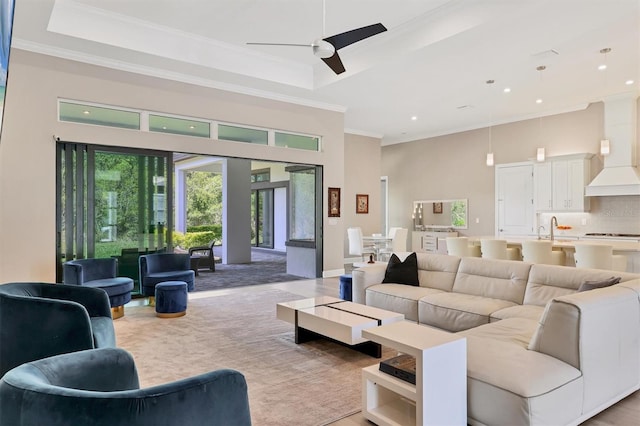 living area featuring a high ceiling, a raised ceiling, ceiling fan, recessed lighting, and ornamental molding