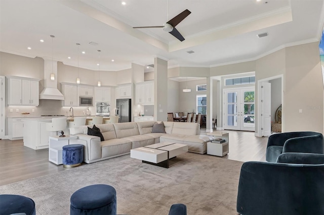 living area with a raised ceiling, light wood finished floors, ceiling fan, crown molding, and recessed lighting