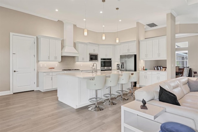 kitchen featuring stainless steel appliances, open floor plan, a sink, ornamental molding, and custom exhaust hood